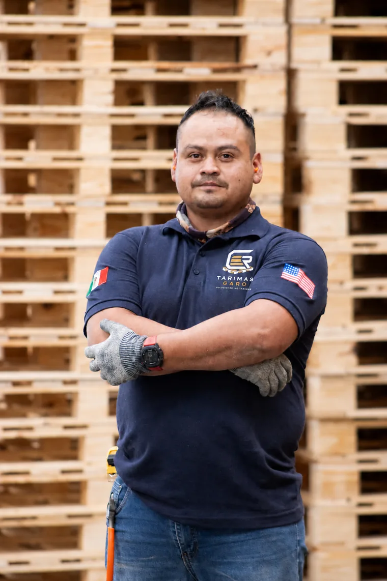Trabajador de Tarimas Garo con guantes frente a un muro de tarimas de madera en el taller de Puebla